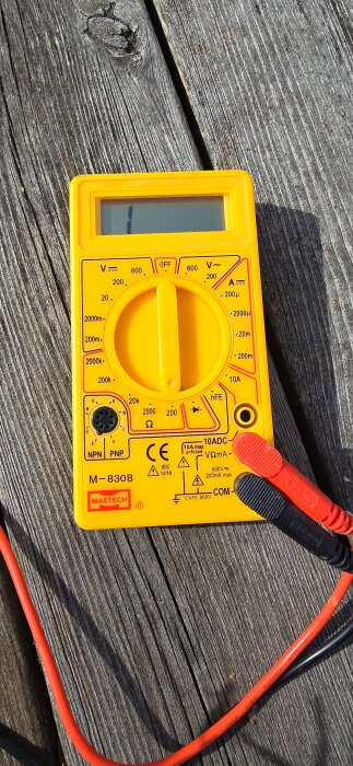 Digital multimeter på träyta, använd för motståndsmätning av faser i ett elektriskt system, med röda och svarta testledningar anslutna.