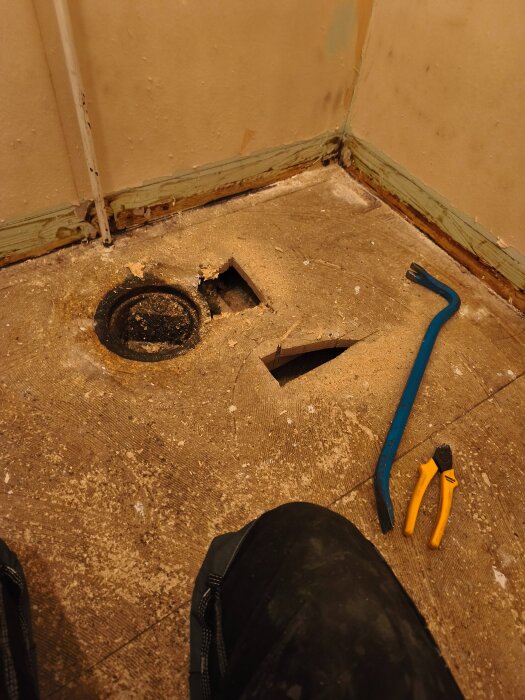 Taxerad grovingång under renovering med golvspån uppbrutet vid brunn, innehåller kofot och tång.