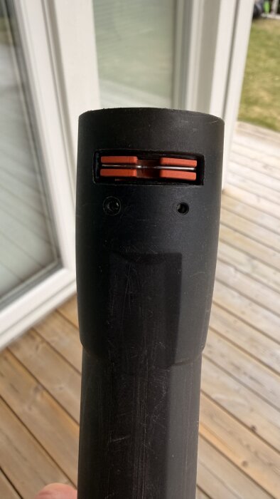 Närbild av en högtryckstvättdel med orange plastfäste, två genomgående hål synliga och en träaltan i bakgrunden.