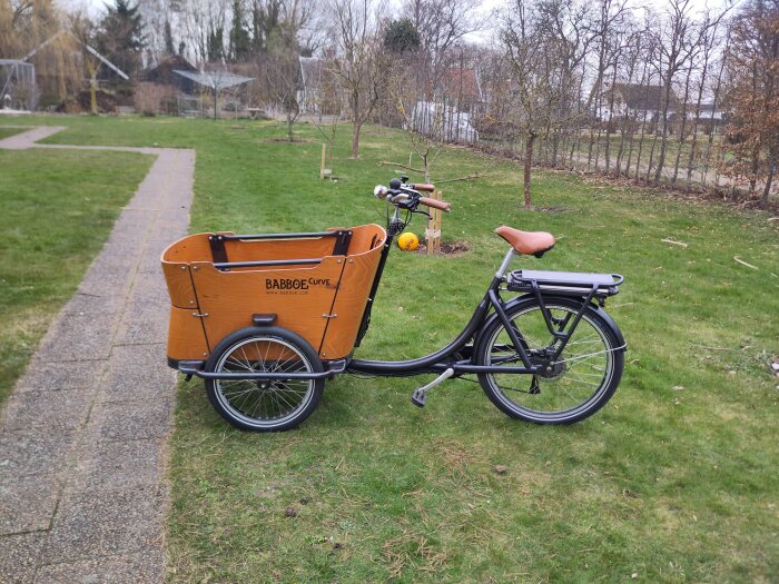 Lådcykel på gräsmatta, nästan färdigbyggd, utan sidobelysning och med träkorg fram.