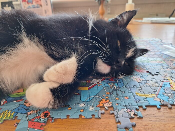 Svartvit katt ligger på ett färgglatt pussel på ett bord.