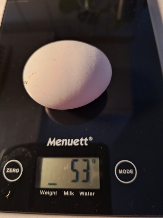 Ett ägg placerat på en digital köksvåg som visar 53 gram.