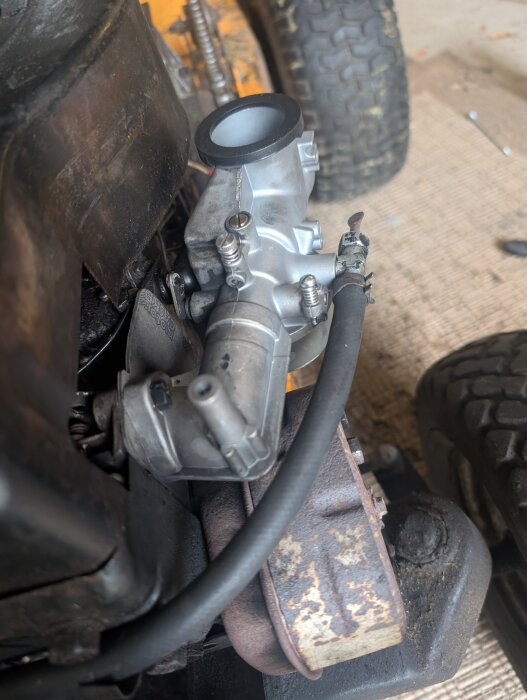 Förgasare på en motor med anslutet bränslerör och synliga delar av en motorcykel eller liten maskin.