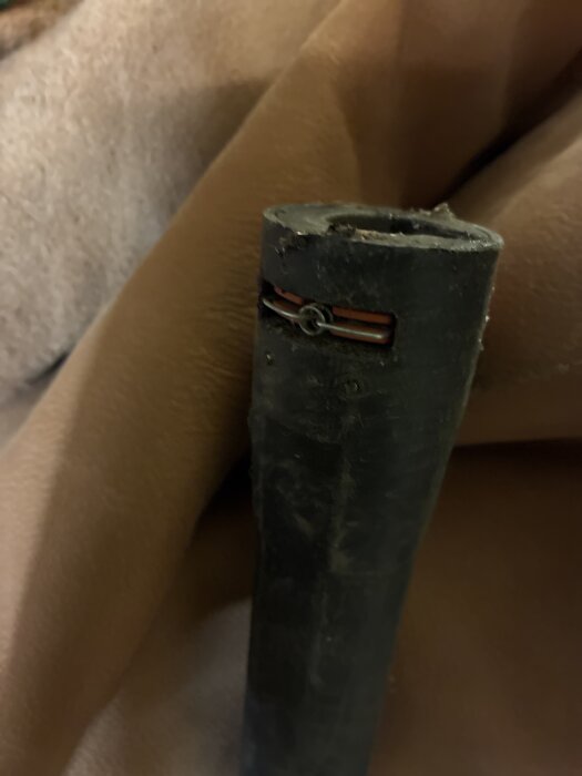 Svart metallstång med en liten fjäder fäst runt toppen, omgiven av brun bakgrundsmaterial.