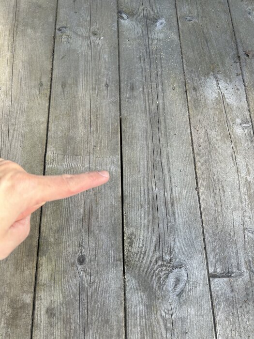 Ett finger pekar på ett smalt mellanrum mellan två grå träplankor på en altan.
