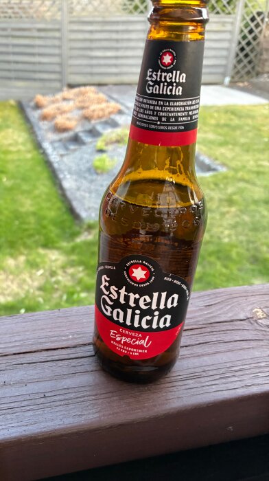 Flaska med Estrella Galicia-öl på en altan, trädgård i bakgrunden.