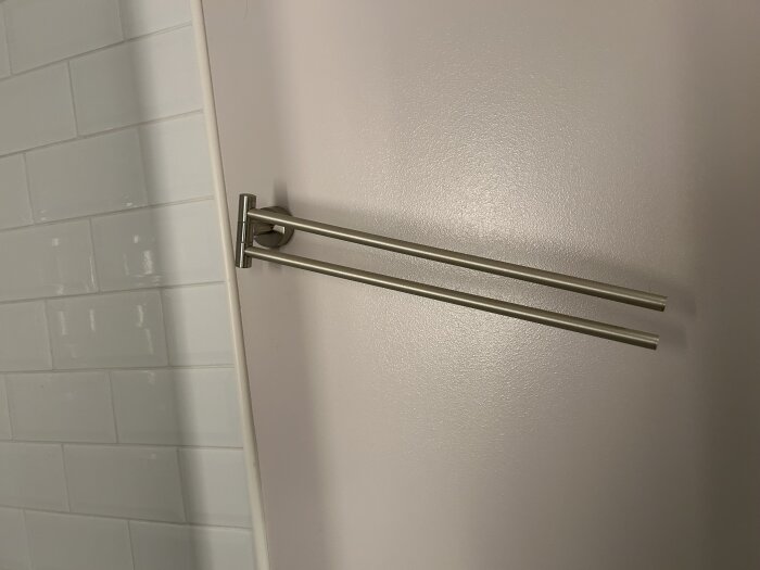 Handdukshängare i metall monterad på vägg i badrum, delvis kaklad.