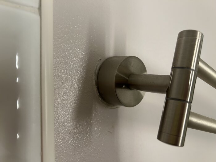 Handdukshängare i metall monterad på en vit badrumsvägg, med synliga monteringsdetaljer bakom.