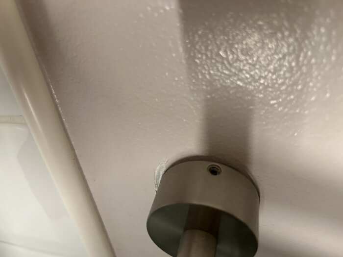 Kromad handdukshängare monterad på en ljus badrumsvägg, visar en infästningspunkt som ska tas bort och hål som eventuellt spacklas igen.