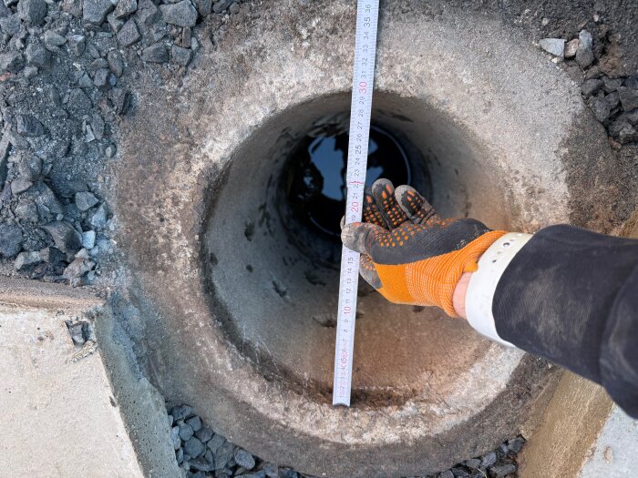 En betongbrunn med en mäthandske och måttband som visar 30 cm i diameter, omgiven av grus och stenmaterial.