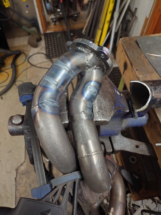Turbo headers i rostfritt stål med svetsade fogar, placerade i ett arbetsrum med verktyg i bakgrunden.