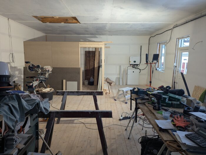 Verkstad under konstruktion med arbetsbänkar, verktyg och byggmaterial. Inredningen är påbörjad med en rumavdelare i bakgrunden.
