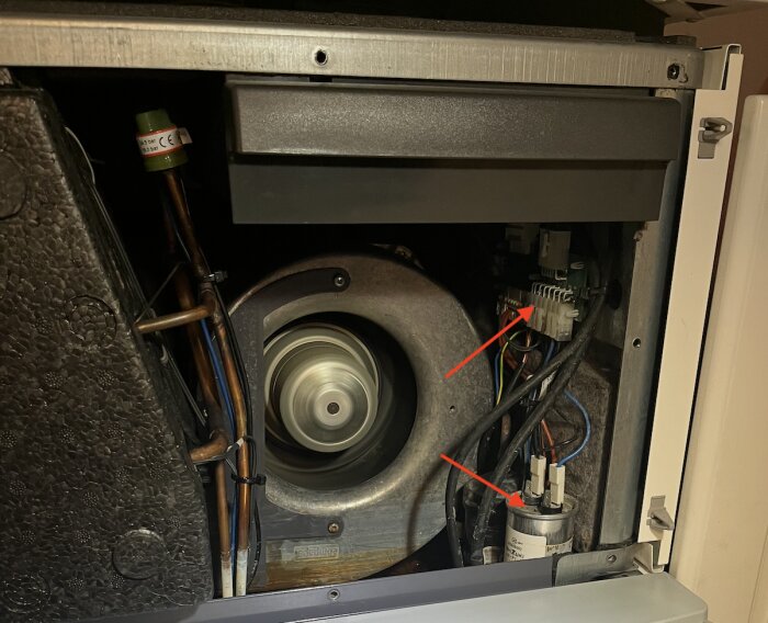Inre del av en ventilationsenhet med synliga kretskort och kablar, markerade med röda pilar som indikerar viktiga komponenter.