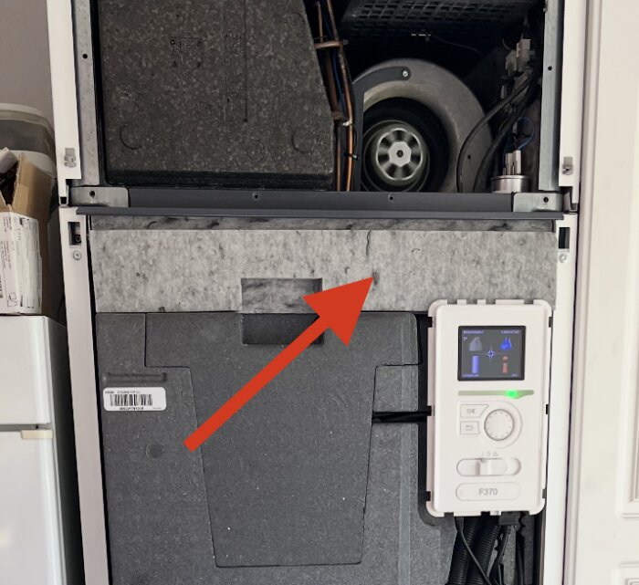 Pannrum med öppen frontpanel visar fläkt och styrsystem, röd pil pekar mot området där kondensvattnet samlas.