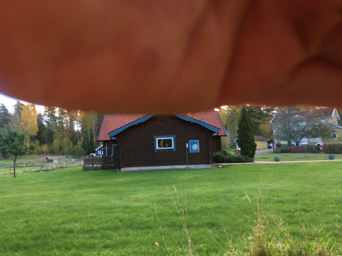 Brunt trähus med rött sadeltak och mönstrade vindskivor, beläget i grönskande landskap.