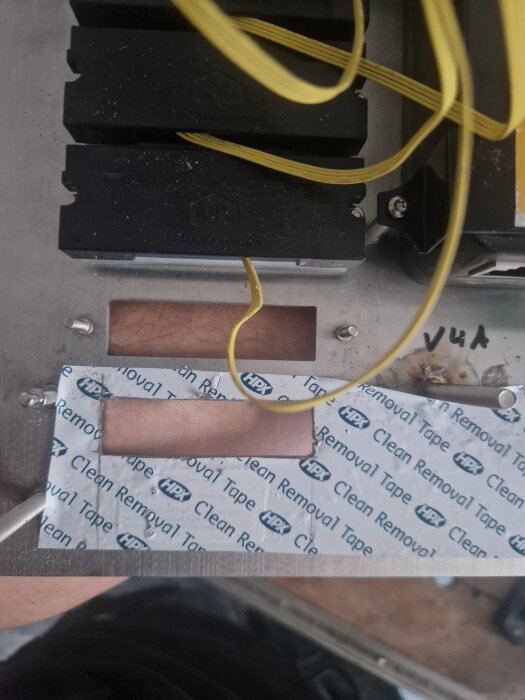 En elektrisk låda med gula kablar och ett urklippt område täckt med HPX Clean Removal Tape, som en del av ett byggprojekt.