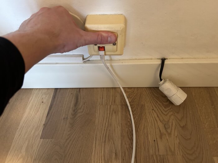 Hand trycker på strömbrytare bredvid eluttag med sladdar.