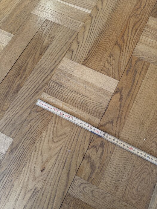 Trägolv i parkettmönster med måttband placerat ovanpå som visar 25 cm.