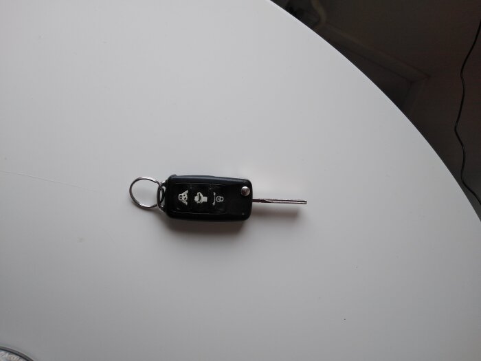 Svart VAG-bilnyckel med utfälld nyckel och sliten knapp, ligger på vitt bord, används för att låsa och låsa upp bilen.