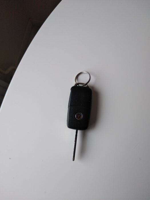 Bilnyckel med svart fjärrkontroll och nyckelring ligger på ett vitt underlag.