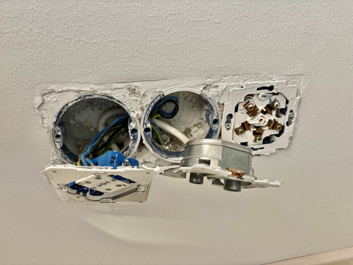 Tre öppna eldosor i en vägg med exponerade kablar, utan utanpåliggande kopplingar på ovansidan. Dosorna är delvis inbyggda i väggen.