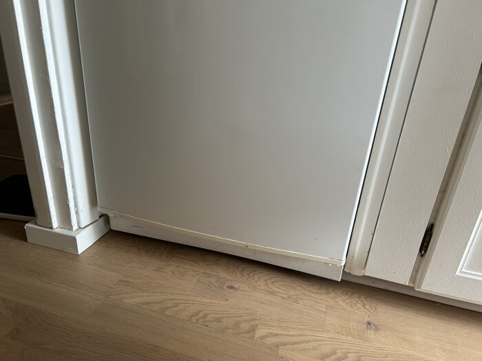 Kyl och frys i ett trångt utrymme med 2 cm glipa mot trägolv, intill en dörrkarm och skåpdörr.