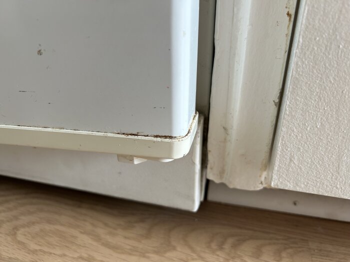 Närbild av en kyl eller frys med liten glipa mot golvet och vägg. Begränsat utrymme runt apparaten.
