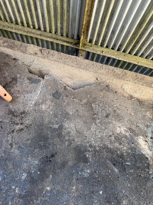 Balkong med gammal stålram och fuktskadad betongyta, delvis täckt av korroderat räcke, visar behovet av renovering och byte till fransk balkong.