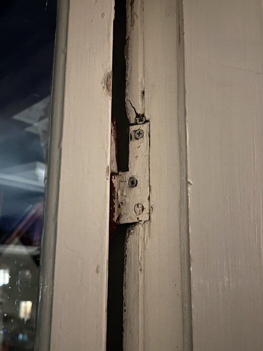 Nära bild av en sliten vit fönsterram med en skadad del och synliga skruvar, redo för reparation.