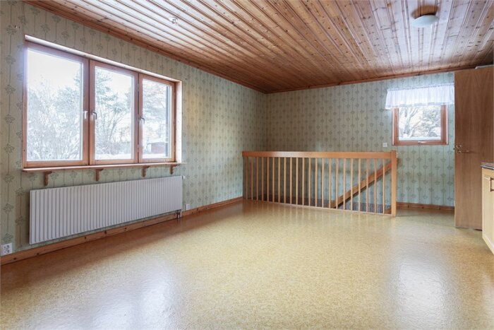 80-talsrum med trätak, tapetserade väggar och gulbrunt golv. Stort fönster, radiator och trappa med trästaket.