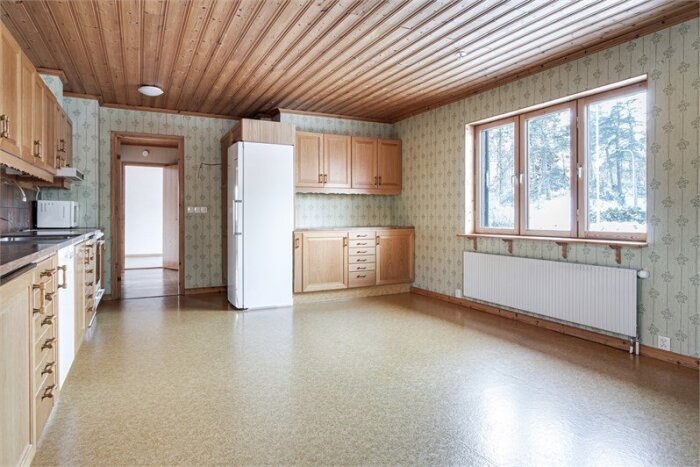 Kök från 1980-tal med trädetaljer och beige golv, träpanel i taket, köksskåp och fönster som visar snötäckt landskap utanför.