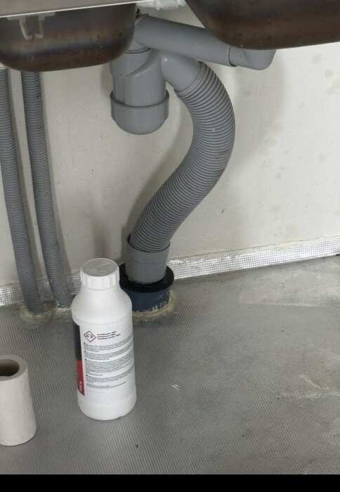 Nyinstallerat laminatgolv med synlig VVS-installation och en flaska kemikalier under diskbänk.