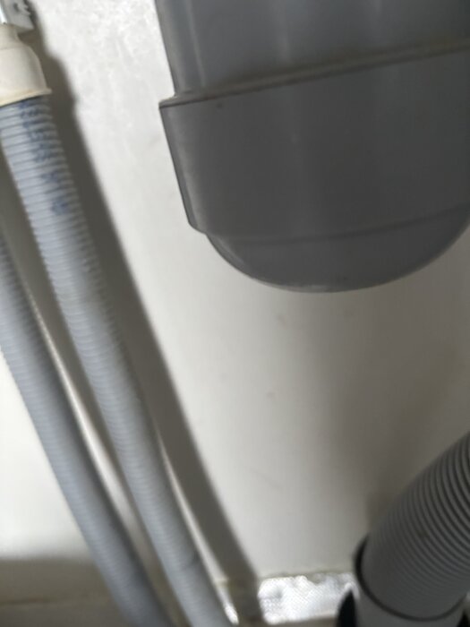 Grå plastslangar och rör mot en vit bakgrund i närbild, sannolikt som del av en bygginstallation.
