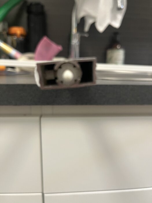 Närbild av ett låsclip i en metallisk ram mot en suddig bakgrund som visar hushållsmaterial.