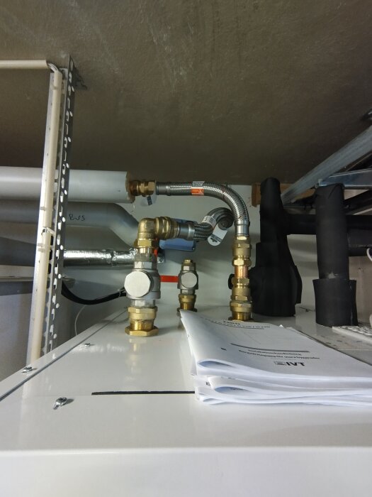Värmepumpsinstallation med bland annat rörkopplingar och flexislangar ovanpå en IVT GEO 228 med dokumentation liggande bredvid.