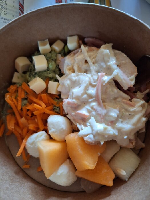 Salladsskål med bitar av ost, strimlad morot, melon, vit dressing och mozzarella över kyckling.