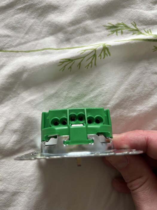 Grön elektrisk kopplingsplint hålls i handen på en vit och grön mönstrad bakgrund.