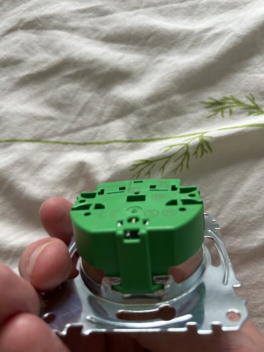 Gröna mekanismen av en elektrisk brytare hålls i en hand ovanpå en vit bakgrund med bladmotiv.
