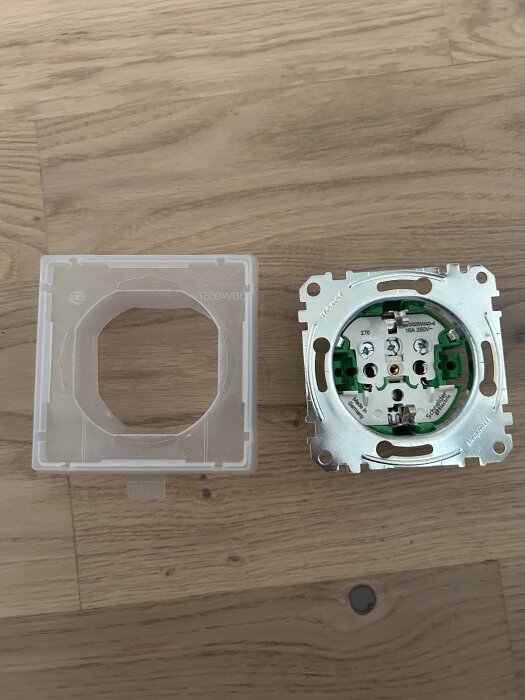 Inbyggd elektrisk väggströmbrytare och plastöverdel ligger på ett trägolv.
