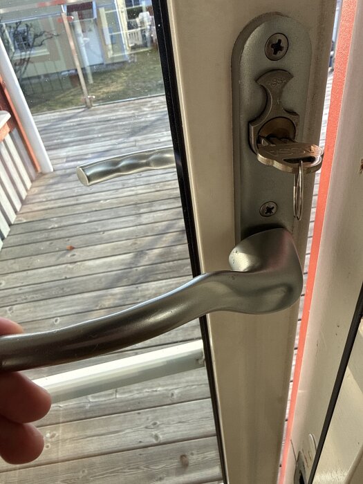 Löst dörrhandtag med exponerade skruvar och ett nyckelhål, fotat inifrån med veranda i bakgrunden.