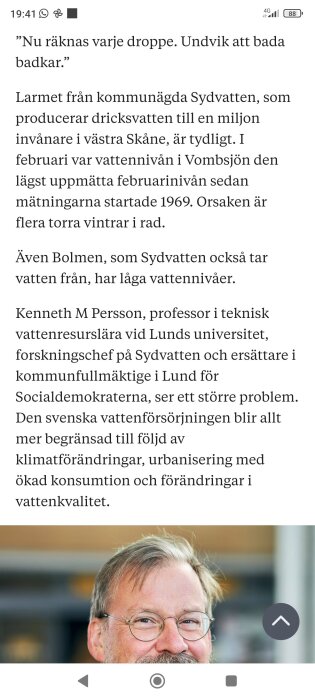 En man med glasögon och skägg ler framför en suddig bakgrund.