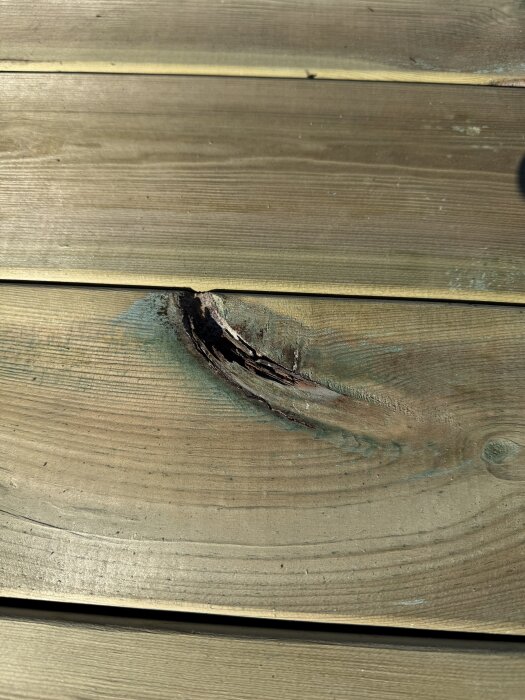 Närbild på en träplanka med en tydlig spricka och ojämnhet, vilket kan indikera sämre kvalitet på materialet.