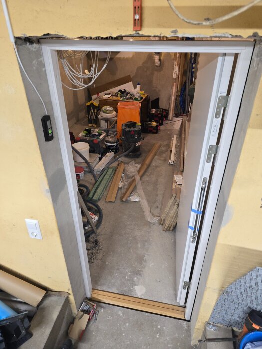 Vit massivdörr i installation, sett från insidan av ett garage. Verktyg och byggmaterial ligger huller om buller på ett betonggolv i bakgrunden.