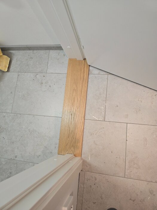 Nyinstallerad dörr med massiv tröskel av ek och ljus dörrkarm, på ett golv med ljusgrå klinkerplattor.