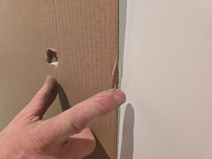 En hand pekar på en skada på en pappförpackning som ser ut att skydda en dörr. Skadan visar ett hål i förpackningen.