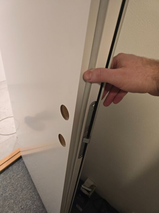 Hand som håller i en massiv dörr vid installation. Dörrbladet har två förborrade hål för lås och handtag. Delen av dörrkarmen med låsuttag syns.