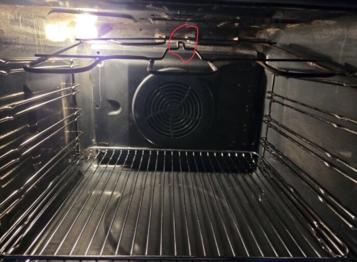 Inuti en ugn med en röd ring runt ett tomt skruvhål på ugnens överdel.