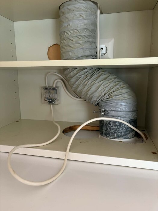 Ventilationskanal med sladdanslutningar i ett köksskåp, visar frånluft och elkopplingar för köksfläkt i behov av renovering.
