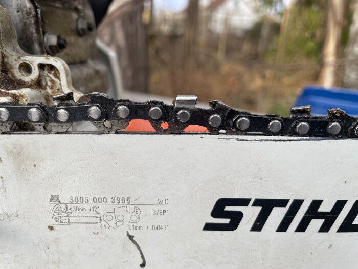 Motorsåg med kedja delvis ur spår på svärdet, visar problem med kedjans spänning och justering. Märkt med Stihl och tekniska specifikationer.