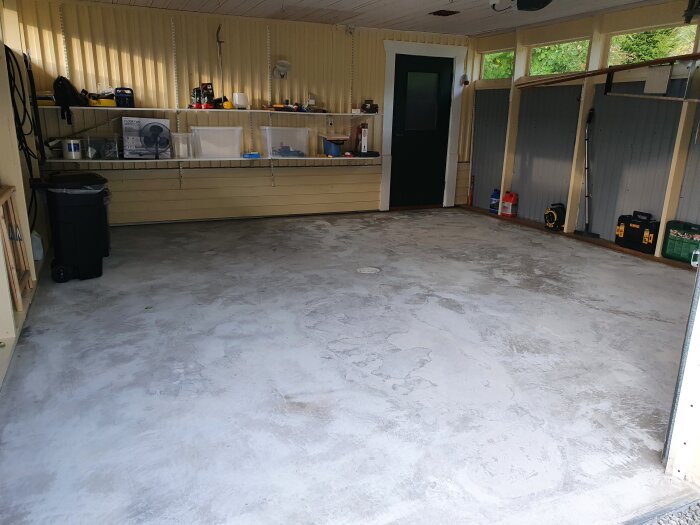 Ren tom garage med betonggolv, hyllor längs väggarna fyllda med verktyg och utrustning.